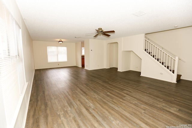 unfurnished living room with arched walkways, dark wood-style flooring, ceiling fan, stairs, and a textured ceiling