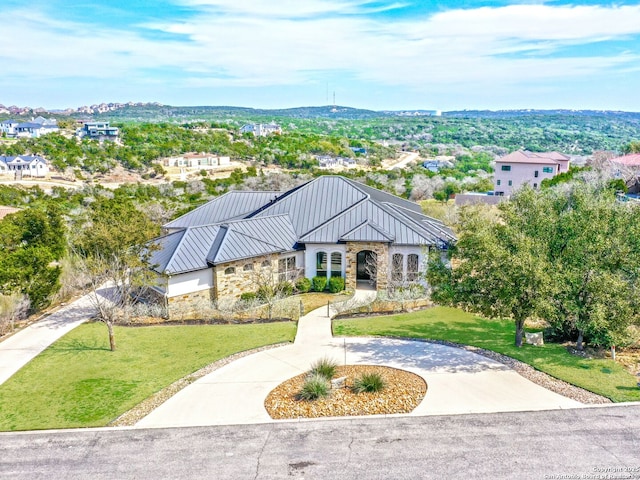 view of front facade featuring curved driveway, a front yard, a standing seam roof, metal roof, and stone siding