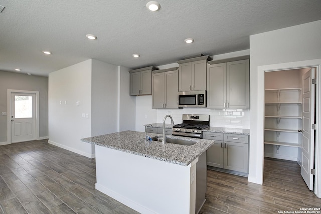 kitchen with light stone counters, gray cabinets, stainless steel appliances, wood finish floors, and backsplash