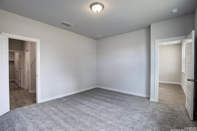 unfurnished bedroom featuring a textured ceiling, carpet, visible vents, and baseboards