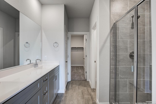 full bath featuring a shower stall, a spacious closet, a sink, and wood finished floors