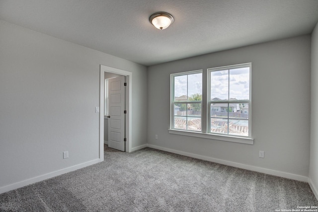 carpeted empty room featuring a textured ceiling and baseboards