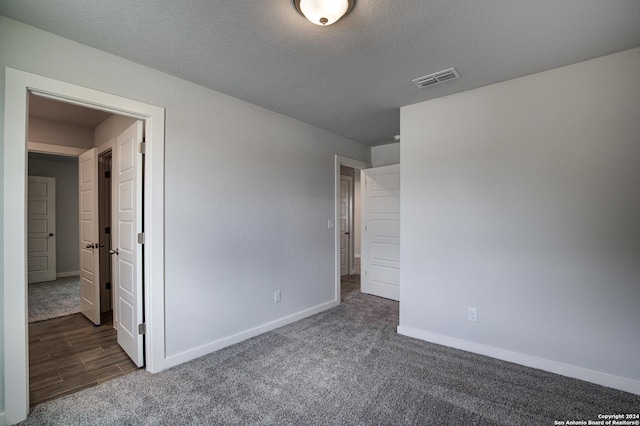 unfurnished bedroom featuring dark colored carpet, visible vents, a textured ceiling, and baseboards