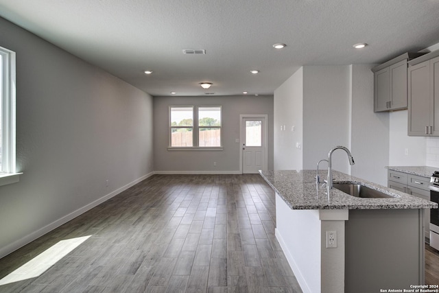 kitchen featuring light stone counters, visible vents, gray cabinetry, a sink, and wood finished floors