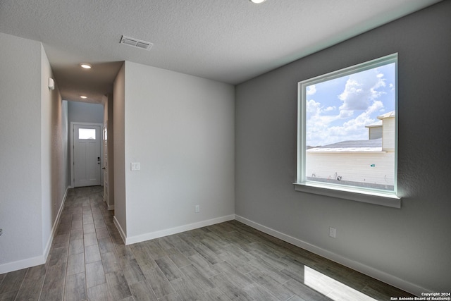 empty room with visible vents, a textured ceiling, baseboards, and wood finished floors