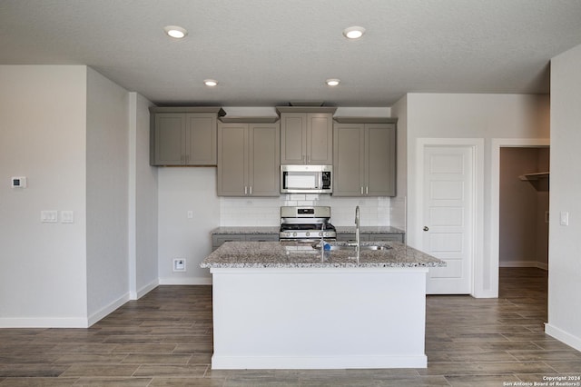 kitchen with a sink, appliances with stainless steel finishes, gray cabinets, and a kitchen island with sink