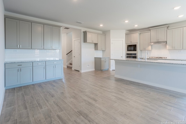 kitchen with stainless steel appliances, tasteful backsplash, visible vents, light wood-type flooring, and under cabinet range hood