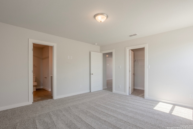 unfurnished bedroom featuring baseboards, visible vents, connected bathroom, light colored carpet, and a spacious closet