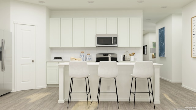 kitchen featuring tasteful backsplash, a kitchen island with sink, stainless steel appliances, light countertops, and a kitchen bar