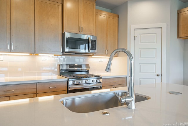 kitchen featuring appliances with stainless steel finishes, light countertops, a sink, and backsplash