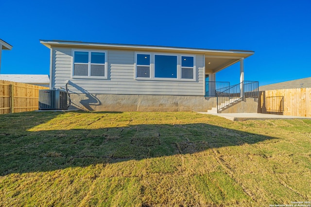 rear view of property with a yard, central AC unit, and fence