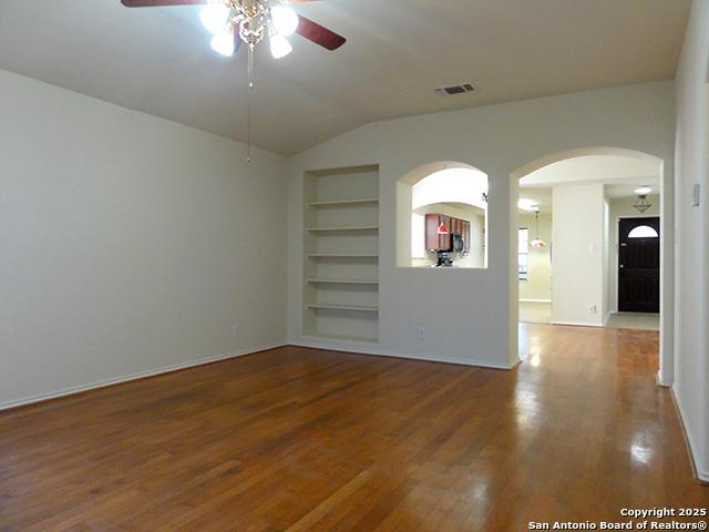 spare room featuring built in shelves, lofted ceiling, visible vents, a ceiling fan, and wood finished floors