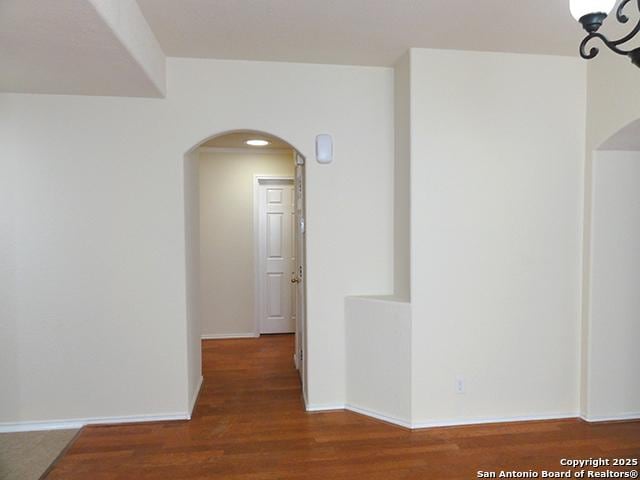 unfurnished room featuring arched walkways, baseboards, and wood finished floors