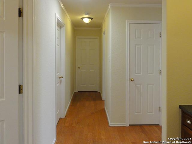 hallway featuring baseboards, crown molding, and light wood finished floors