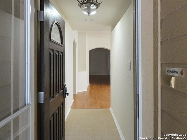 corridor with arched walkways, baseboards, and light tile patterned floors