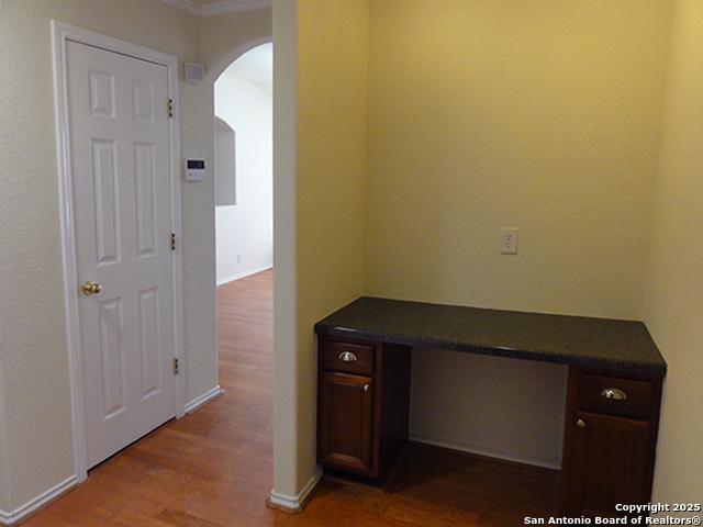 unfurnished office featuring arched walkways, built in desk, and wood finished floors