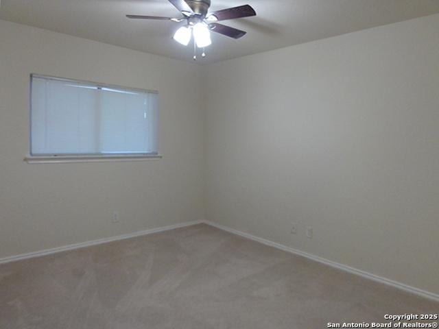 carpeted spare room featuring ceiling fan and baseboards