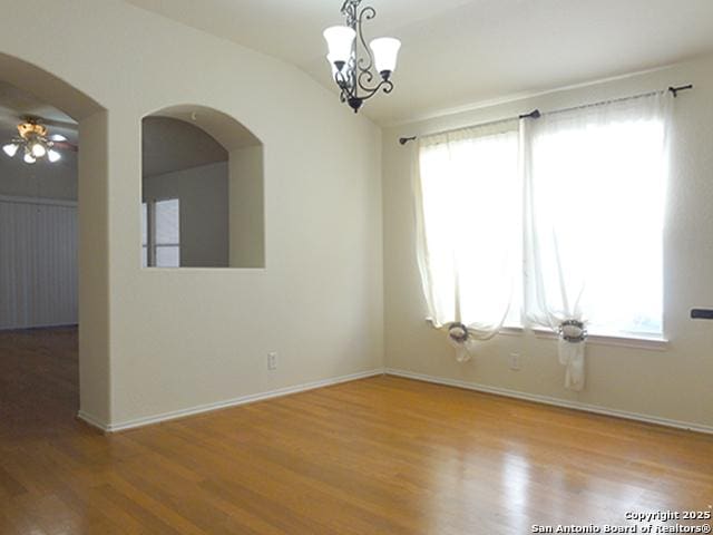 unfurnished room with lofted ceiling, baseboards, an inviting chandelier, and wood finished floors