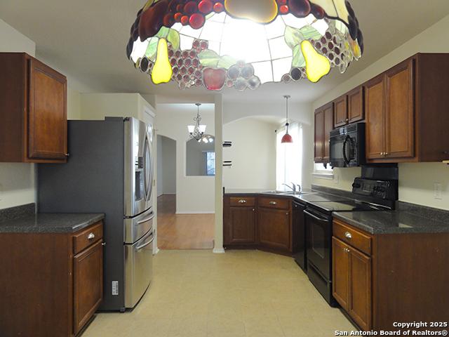 kitchen with black appliances, dark countertops, a sink, and an inviting chandelier