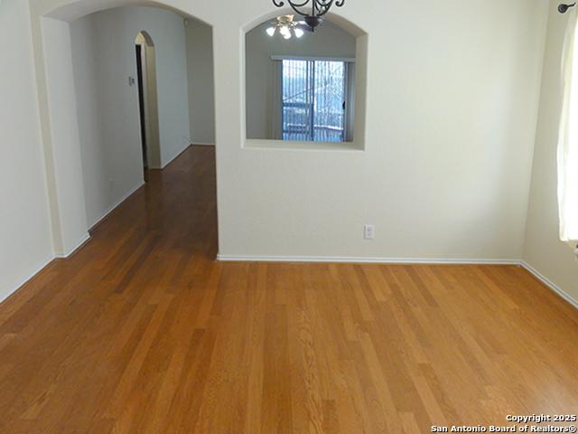 unfurnished dining area with a wealth of natural light, arched walkways, a notable chandelier, and wood finished floors