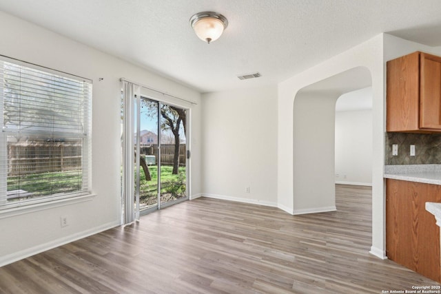 unfurnished dining area with arched walkways, a textured ceiling, wood finished floors, visible vents, and baseboards