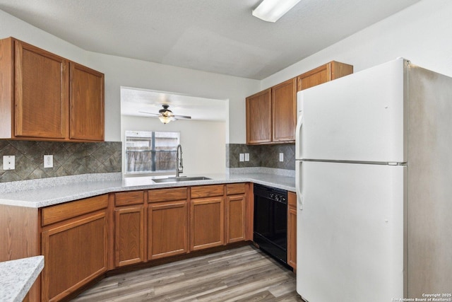 kitchen with light wood finished floors, black dishwasher, freestanding refrigerator, light countertops, and a sink