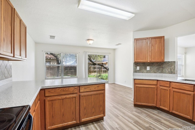 kitchen with a peninsula, brown cabinetry, light wood-style flooring, and light countertops