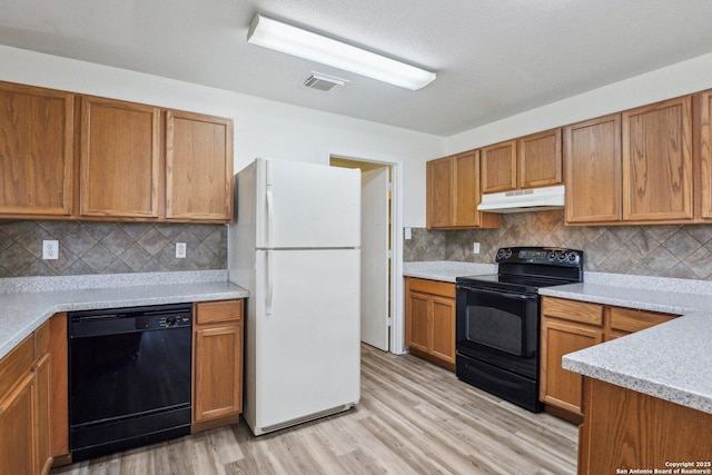 kitchen with black appliances, brown cabinetry, visible vents, and under cabinet range hood