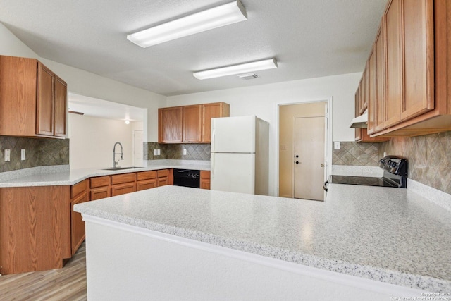 kitchen featuring under cabinet range hood, a peninsula, range with electric stovetop, a sink, and freestanding refrigerator