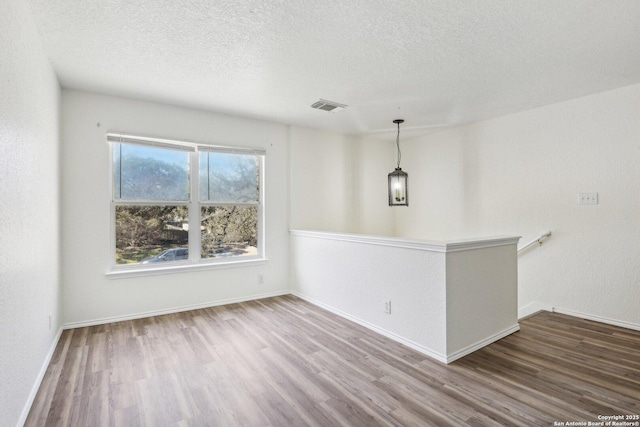 empty room featuring a textured ceiling, wood finished floors, visible vents, and baseboards