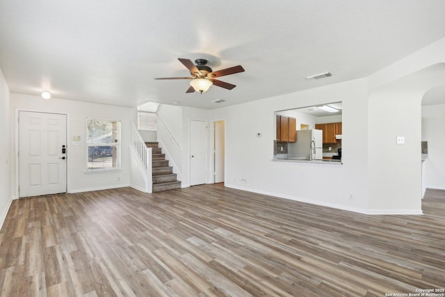 unfurnished living room featuring arched walkways, visible vents, stairway, ceiling fan, and wood finished floors