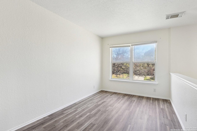 unfurnished room featuring visible vents, a textured wall, a textured ceiling, wood finished floors, and baseboards