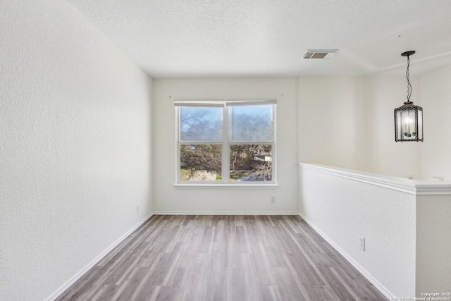 spare room featuring a textured ceiling, a textured wall, wood finished floors, and baseboards