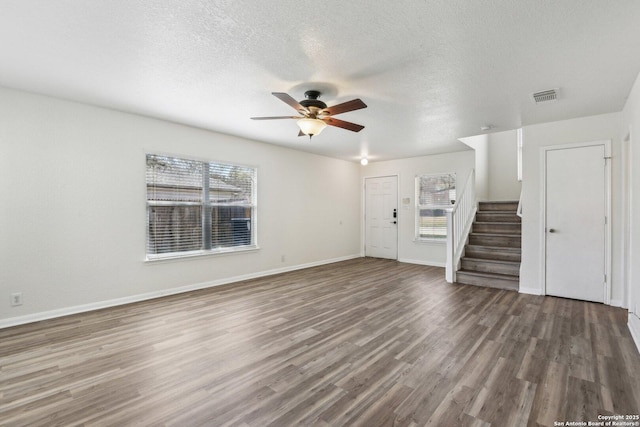 unfurnished living room with stairs, visible vents, a wealth of natural light, and wood finished floors