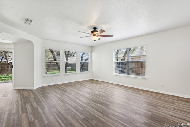 unfurnished room with plenty of natural light, a textured ceiling, visible vents, and wood finished floors