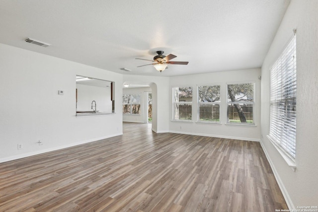 unfurnished living room with a wealth of natural light, arched walkways, visible vents, and wood finished floors