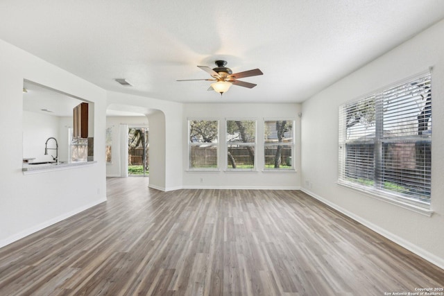 unfurnished living room with arched walkways, visible vents, a textured ceiling, wood finished floors, and baseboards