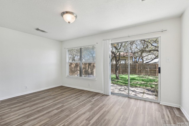 unfurnished room featuring plenty of natural light, a textured ceiling, visible vents, and wood finished floors