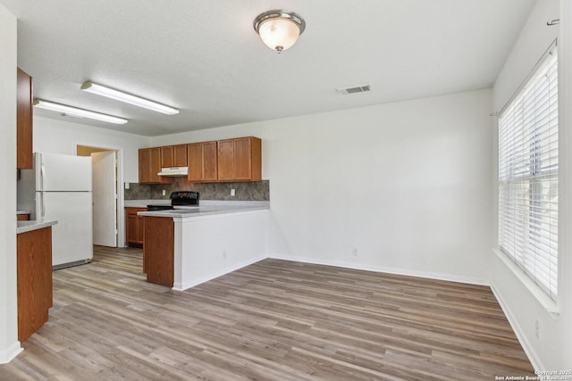 kitchen with a peninsula, visible vents, freestanding refrigerator, black electric range oven, and brown cabinetry