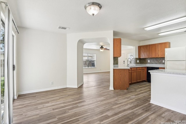 kitchen with light countertops, backsplash, freestanding refrigerator, brown cabinets, and dishwasher