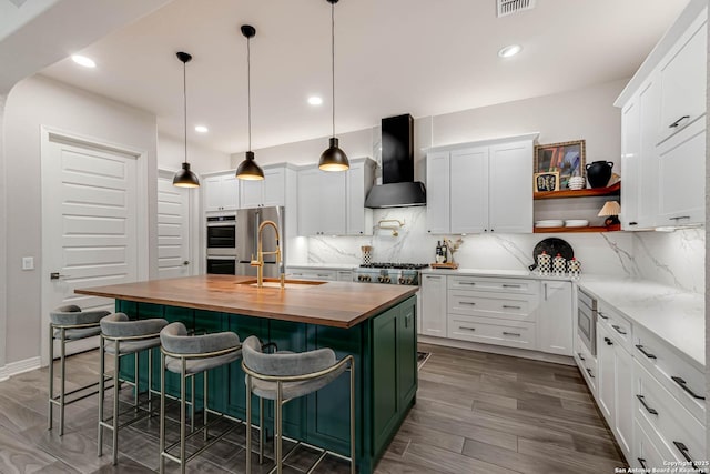 kitchen featuring decorative backsplash, white cabinetry, a sink, wall chimney range hood, and butcher block countertops