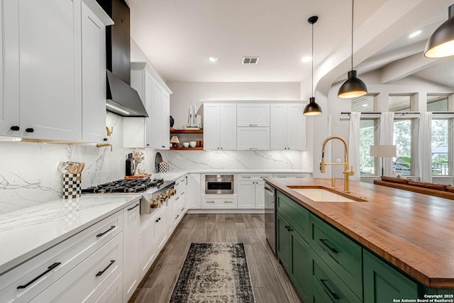 kitchen featuring a sink, wood counters, appliances with stainless steel finishes, wall chimney exhaust hood, and green cabinetry