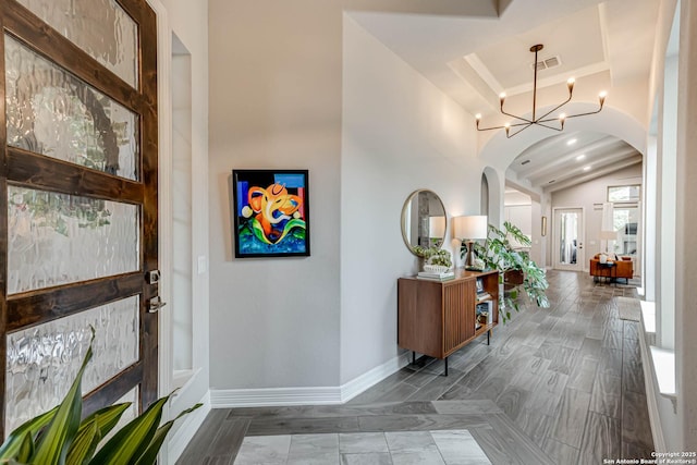 entrance foyer featuring arched walkways, a chandelier, visible vents, baseboards, and vaulted ceiling