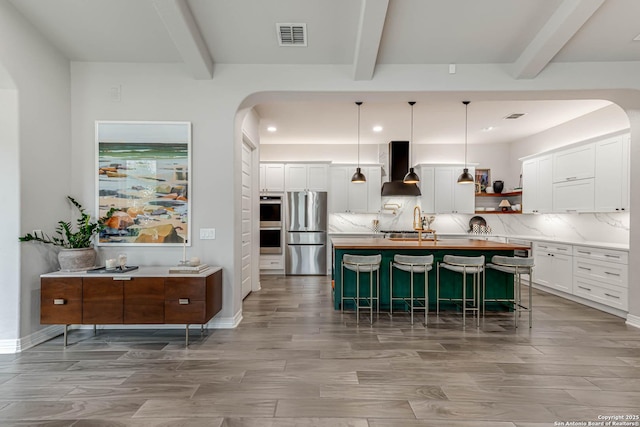 kitchen with wall chimney range hood, open shelves, decorative backsplash, and freestanding refrigerator