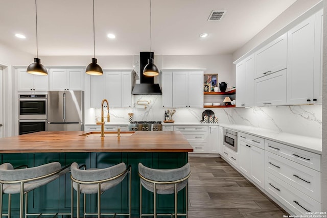 kitchen with visible vents, wood counters, stainless steel appliances, wall chimney range hood, and a sink