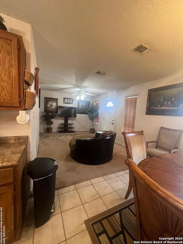 living area with a textured ceiling, light tile patterned floors, light colored carpet, a ceiling fan, and visible vents