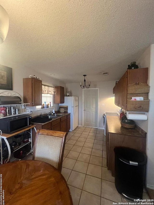 kitchen featuring light tile patterned floors, a sink, freestanding refrigerator, brown cabinetry, and an inviting chandelier