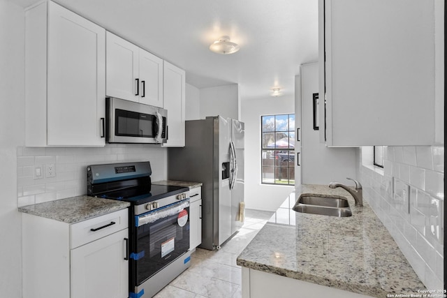 kitchen featuring stainless steel appliances, a sink, white cabinetry, and light stone countertops