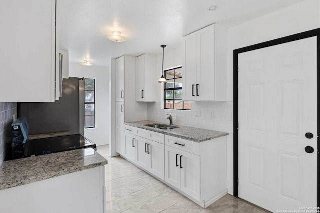 kitchen featuring decorative backsplash, stove, light stone counters, and a sink