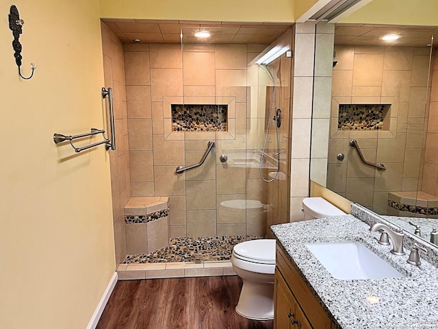 full bathroom featuring toilet, a tile shower, vanity, wood finished floors, and baseboards